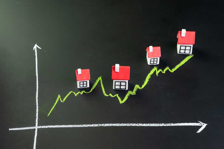 House, property or real estate market price go up or rising concept, small miniature house with green line graph going up on black chalkboard