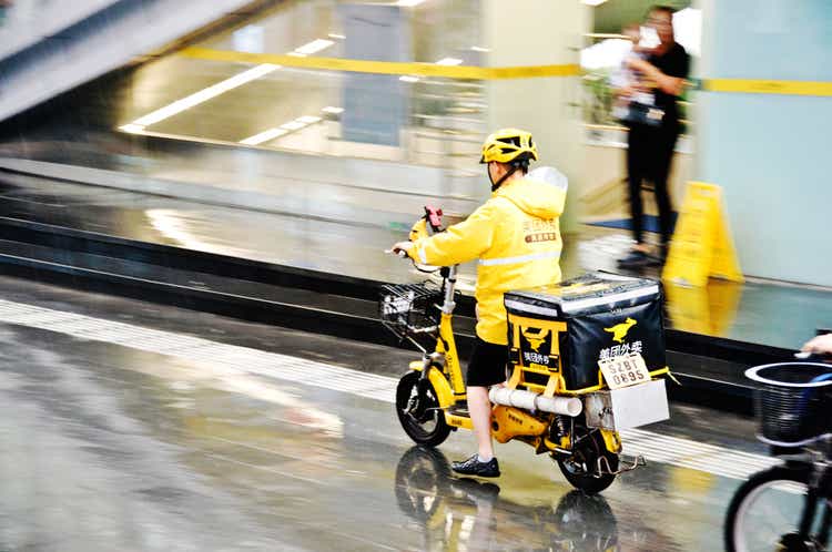 Meituan food delivery worker on motorcycle in the rain in Futian Business District, Shenzhen - China. Founded by Wang Xing, the app is used in China for food delivery, restaurant deals, movie tickets, hotel, travel bookings, etc