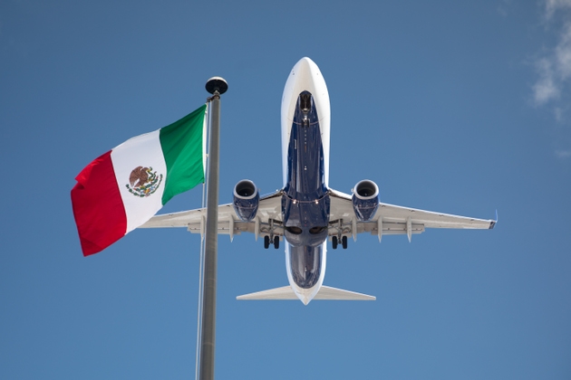Bottom View of Passenger Airplane Flying Over Waving Mexico Flag On Pole