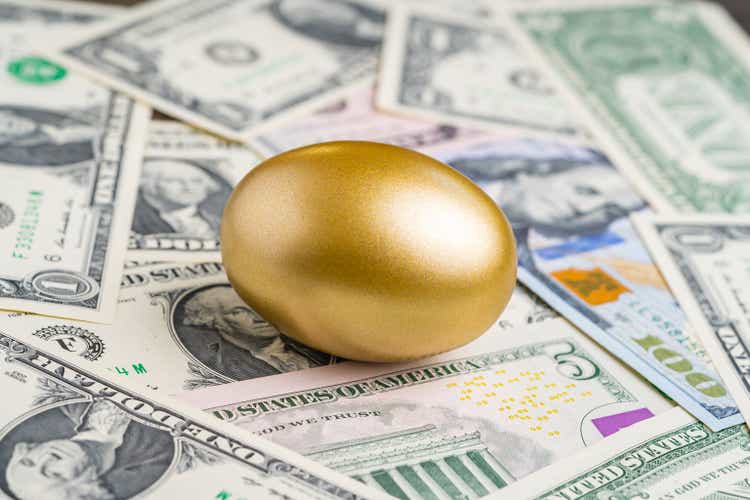 Shiny golden egg on pile of US America dollar banknotes money metaphor of finding the unbelievable good stock with high dividend or success investment in stock market concept