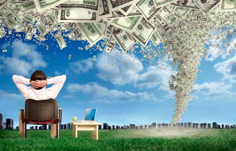 businessman sitting on green landscape with laptop computer looking at city view with storm of money