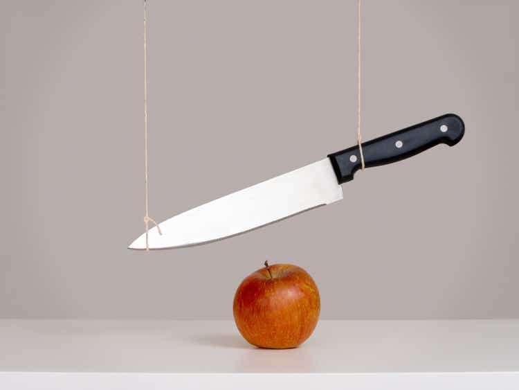 Sword of Damocles threat, risk concept, metaphor - large knife tied and suspended over apple. Still life.
