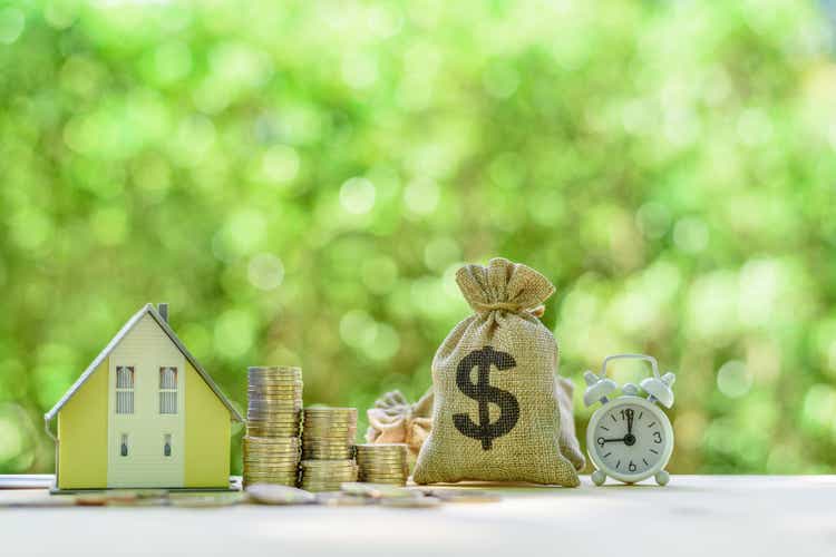 Mortgage-backed security MBS, financial concept : House model, stacks of rising coins, US dollar, money bags, a clock on a table over green background, depicts investment in home bought from the bank