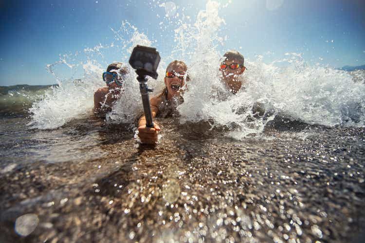 Kids playing in sea waves and filming themselves using waterproof action camera.