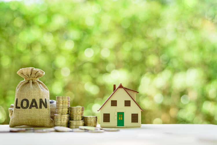 Mortgage-backed security MBS, financial concept : House model, stacks of rising coins, loan bags on a table over green background, depicts raising fund from a bank to buy home or properties or assets