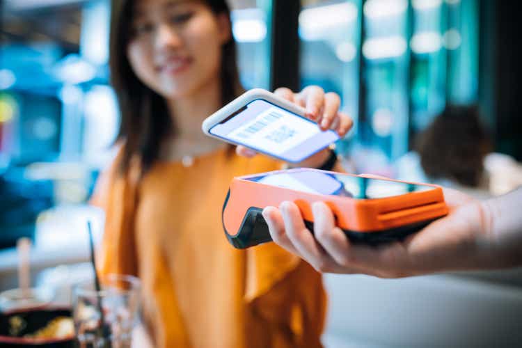 Asian young woman paying with smartphone in a cafe.