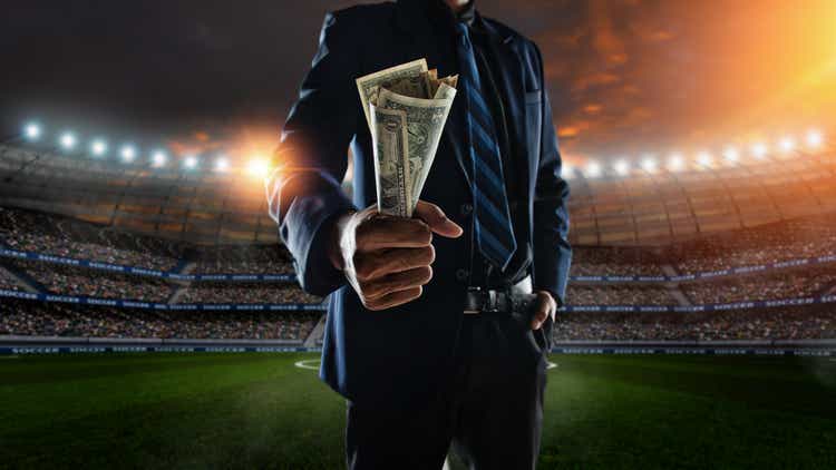 businessman holding large amount of bills at Soccer stadium in background