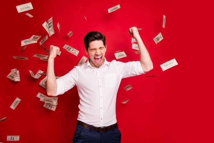 Photo of ecstatic overjoyed man rained with bucks banknotes achieving success while isolated with red background