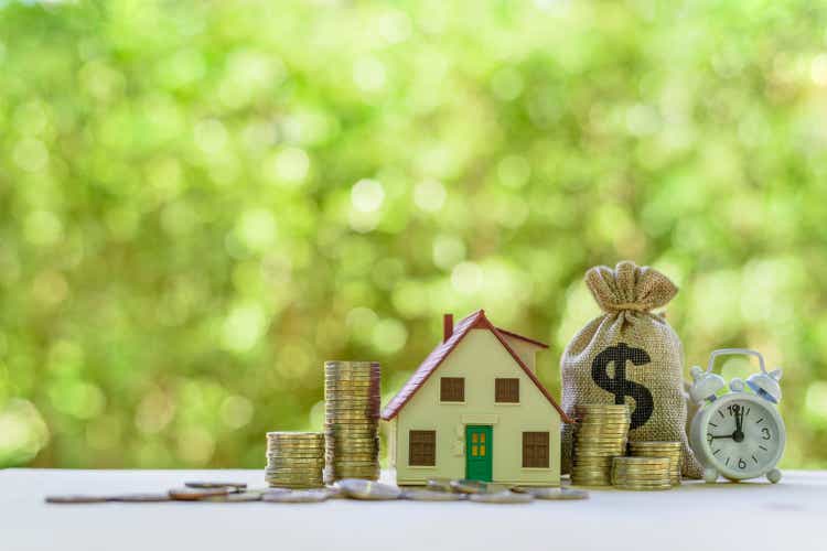 Residential real estate loan, financial concept : House model, coins, US dollar bag, white clock on a table, depicts home loan or borrowing money to buy / purchase a new home for first time homebuyer