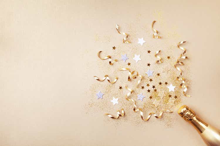 Champagne bottle with confetti stars, glitter and party streamers on golden background. Christmas, birthday or wedding concept. Flat lay concept.