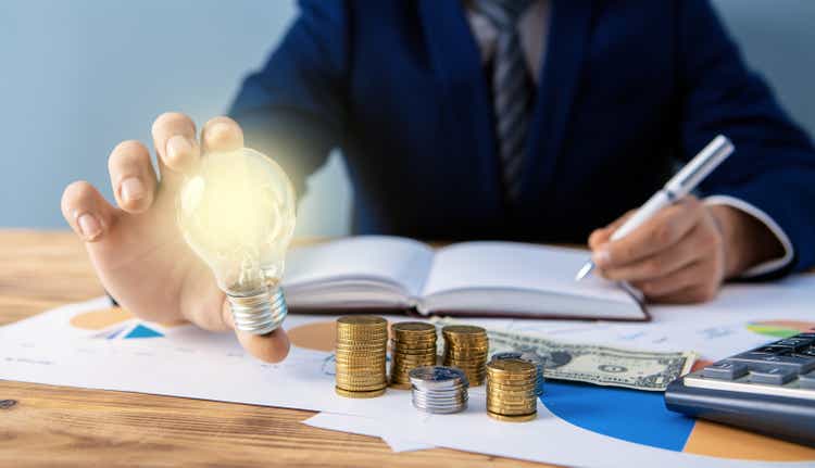 businessman in the office, with one hand doing the calculations with the other holds a lamp, a symbol of the idea; The idea of saving energy and accounting finances