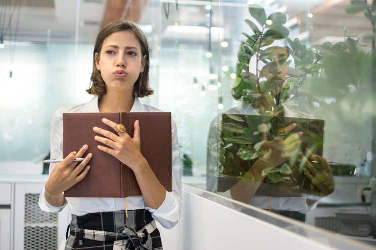 Portrait of beautiful young business woman pouting and holding notebook in office