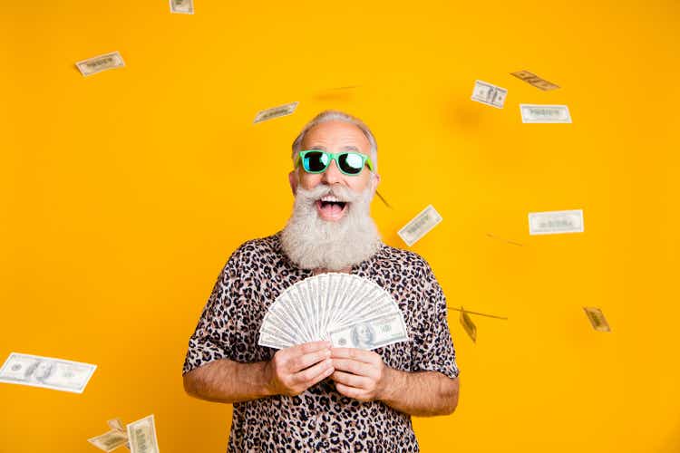 Photo of elderly old confident rich man holding banknotes in his hands and being rained with currency while isolated with yellow background