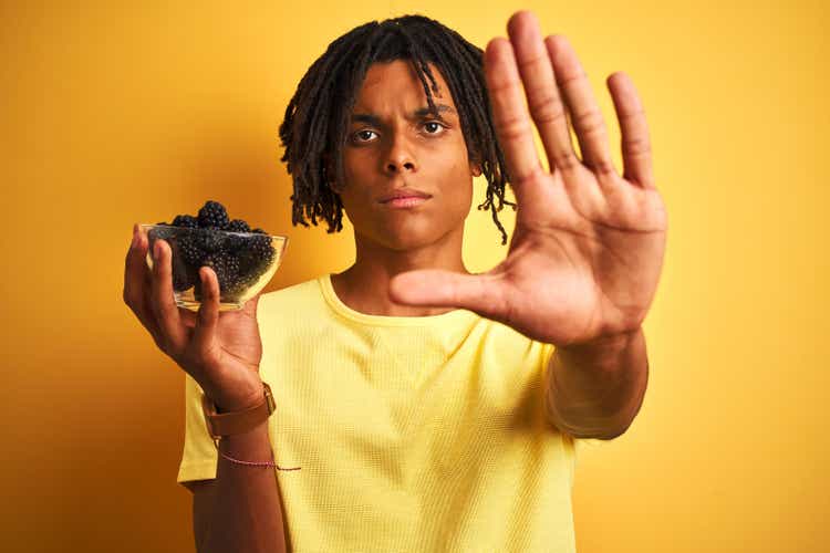 African american man with dreadlocks holding blackberry over isolated yellow background showing stop sign with open hands, serious and confident expression, defensive gesture