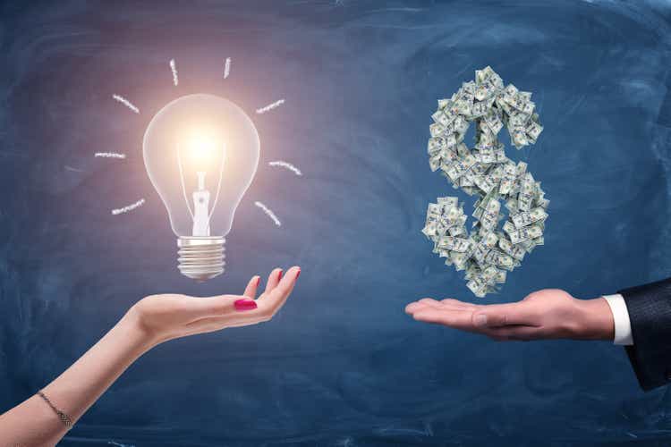 A female and a male hands holding a large bright light bulb and a dollar sign made of many money bills.