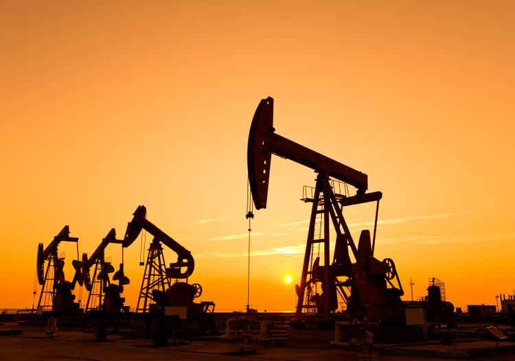 Oil pumps and drilling rig at sunset