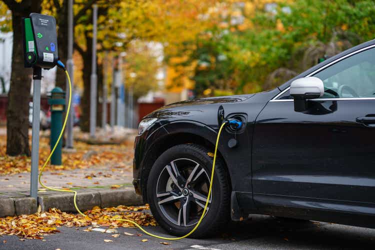 Volvo car is plugged in for charging on street parking lot with beautiful autumn view background