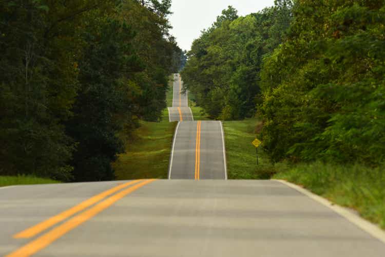Low-angle view down stiped two-lane road over hilly terrain through pine forest