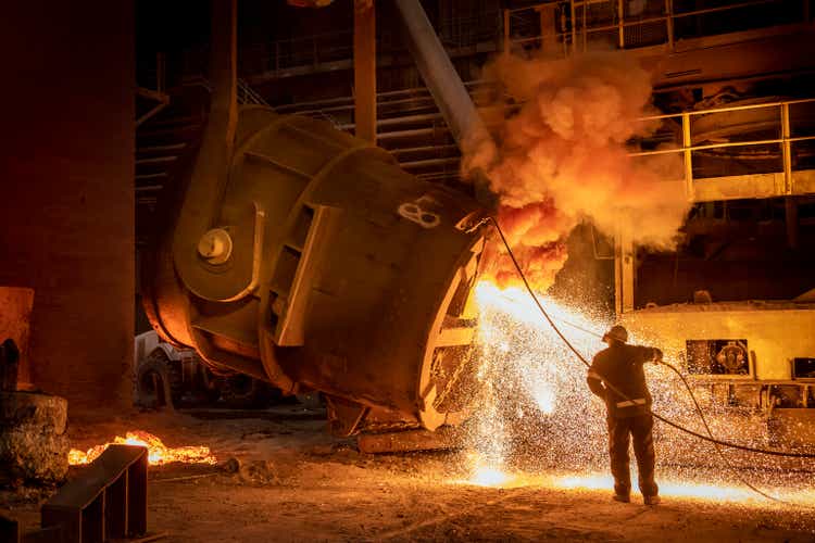 Steelworker cleaning pouring end of flask during steel pour in steelworks