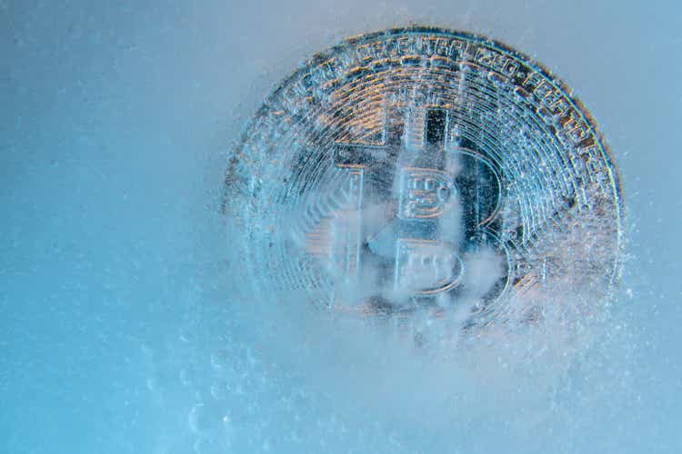 Silver Bitcoin, bit coin online digital currency frozen in the blue ice. Concept of block chain, crypto market crash. Frozen crypto money, depreciation