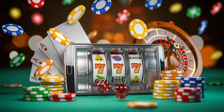 Online Casino.  Smartphone or mobile phone, slot machine, dice, cards and roulette on a green table in the casino.  3d