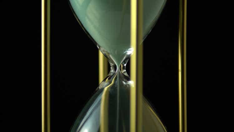 Still hourglass clock time concept. Old vintage gold metal frame green sand clock countdown on dark background. Close up.
