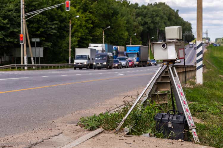 mobile speed camera device on tripod working on summer daytime road with blurry traffic in background