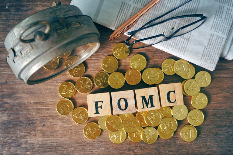 Top view wood cube which have text "FOMC" decorate with gold coins near old clock and pen and glasses on the newspaper,econimic data concept.