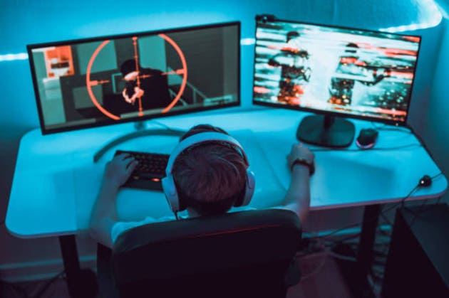 Boy plays video game online and sits in front of two big computer monitors
