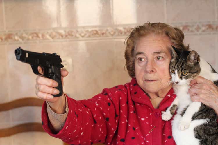Angry senior woman protecting her cat with a gun
