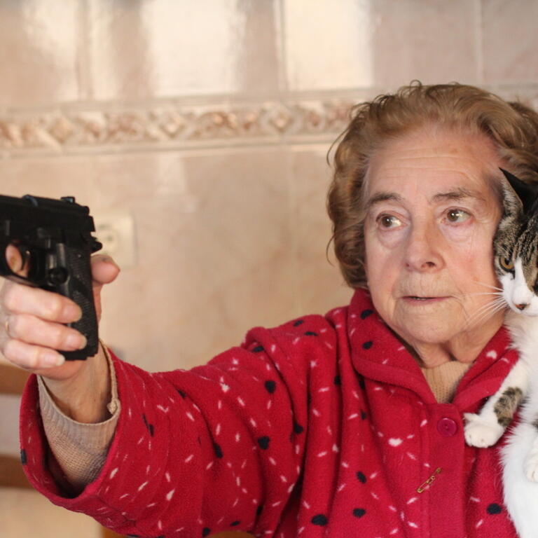 Angry senior woman protecting her cat with a gun