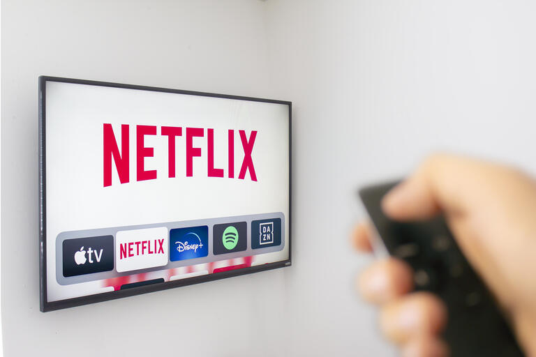 A Person holds an Apple TV remote using the new Netflix app with a hand. Netflix dominates Golden Globe Nominations. Illustrative