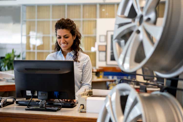 Beautiful woman working at reception desk in auto repair shop looking at computer screen very cheerfully