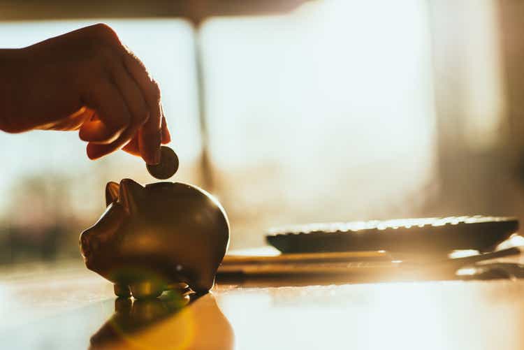 Putting a coin in a gold colored piggy bank at home.