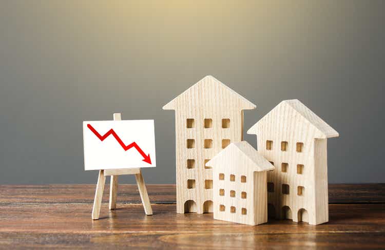 Wooden houses residential buildings and an easel with a red down arrow. Fall of real estate market. Value cost decrease. Bad liquidity attractiveness. Cheap rent. Reduced demand, recession. Low sales