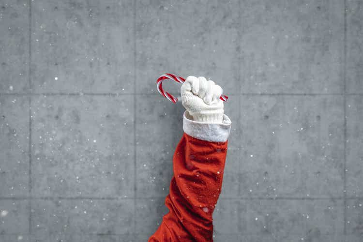arm of santa claus raised up and holding a candy cane in front of concrete wall