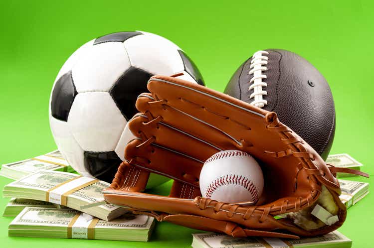 Winning bet on sporting event, money in sport and sports betting conceptual idea with baseball glove, football, soccer ball and wad of cash isolated on green background