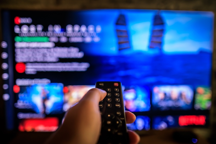 TV remote control in the foreground, Video on demand screen in the blurry background