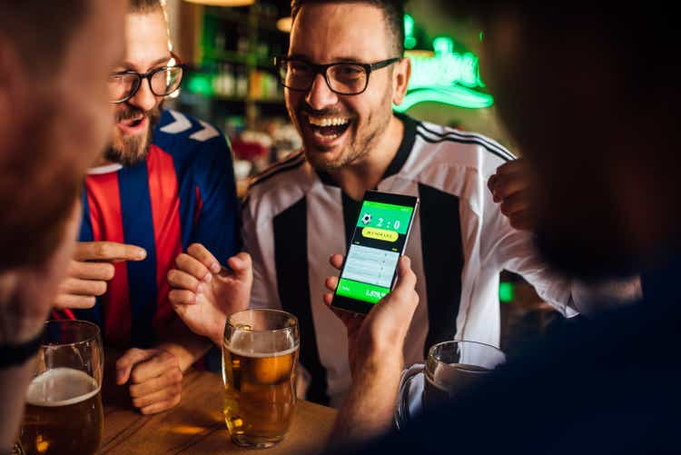 Friends drinking beer, watching soccer game and using mobile app for betting