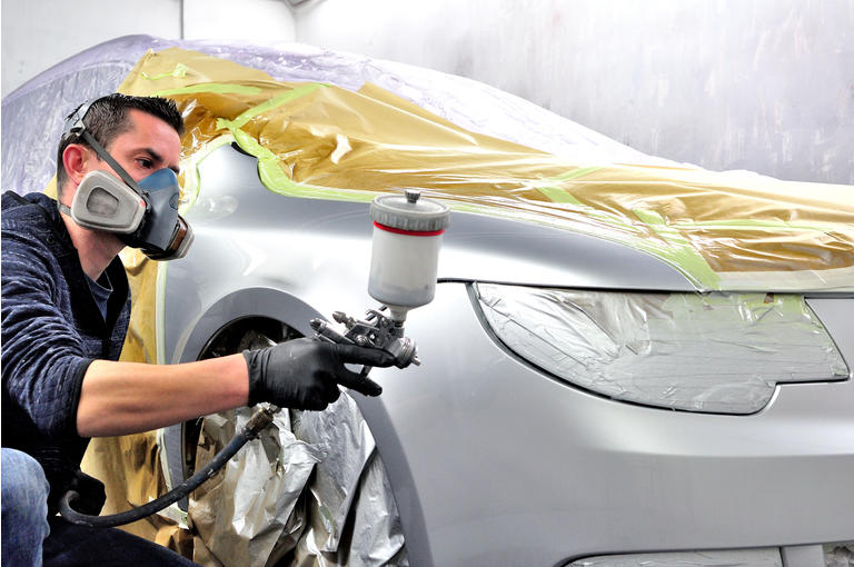 Professional male painting silver car.
