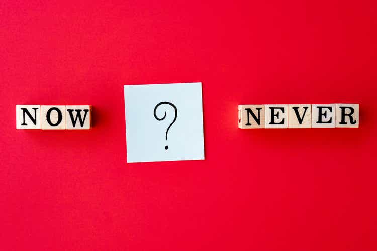 now or never concept with text on wooden blocks and question mark on red background