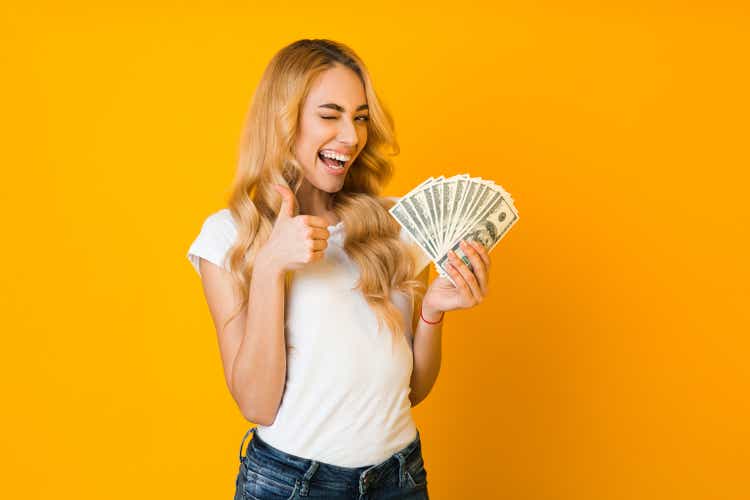 Cashback. Excited woman holding money banknotes and showing thumb up