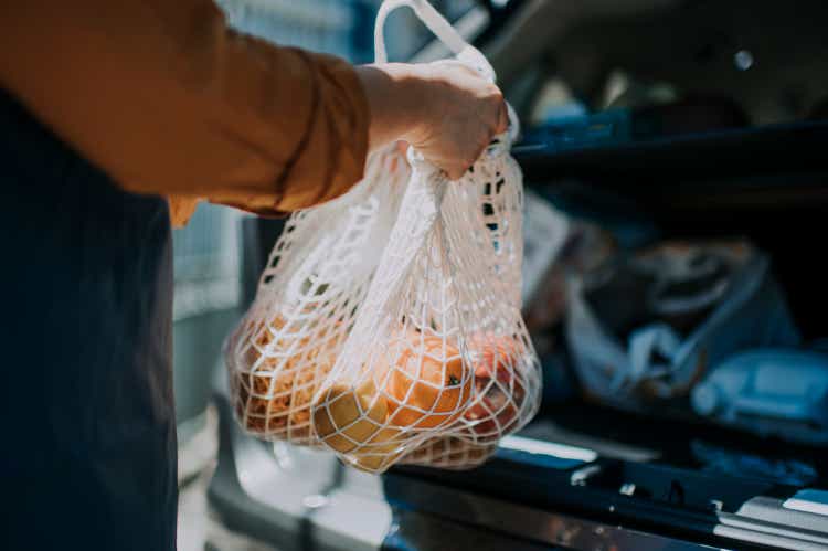 an asian chinese female delivery person getting the groceries and fruit her customer order online shopping in recycle bags from her car trunk and deliver it to her customer
