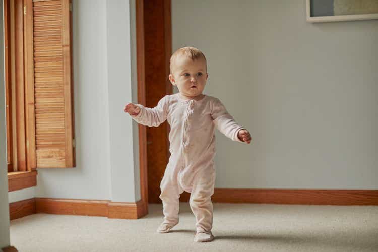 Baby first steps walking in bedroom with arms out with good balance