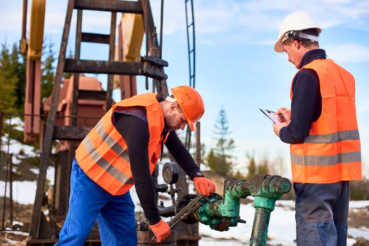 Oil workers in uniforms controlling progress work at local oil pump station on sunny day