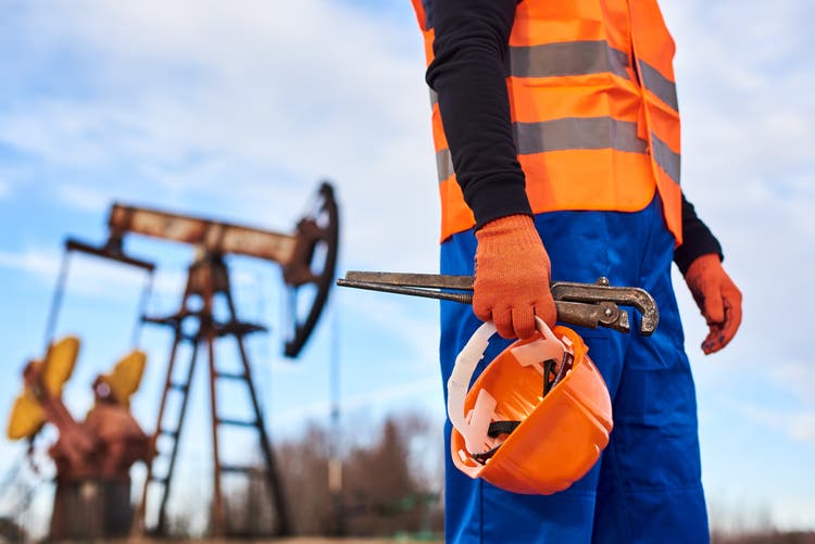 Oil worker in orange uniform and helmet on of background the pump jack and blue sky.