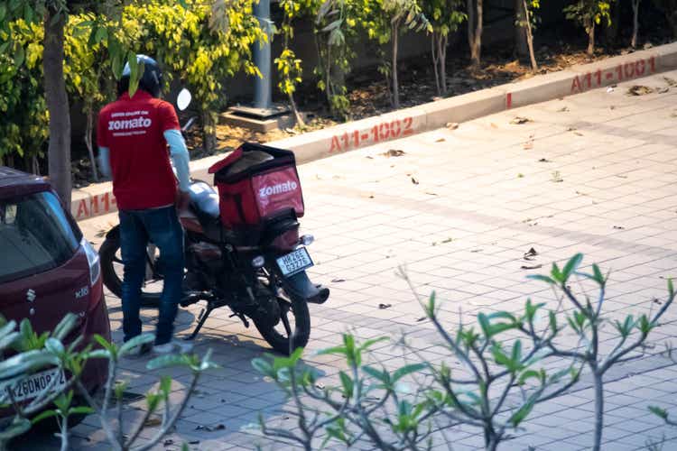 Zomato delivery person wearing the red shirt waiting near his bike with the zomato delivery bag