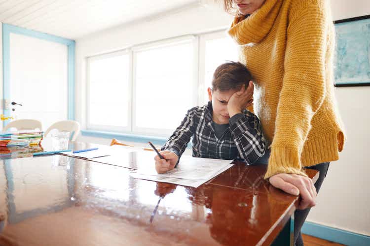 Madre viendo hijo frustrado haciendo la tarea en la mesa de comedor