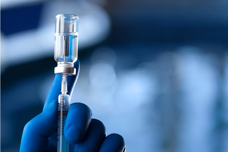 A medical hand in a glove holds an ampoule with a vaccine and a syringe with illustration