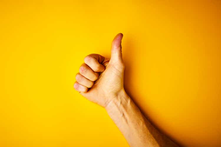 Hand making thumbs up signal on yellow background